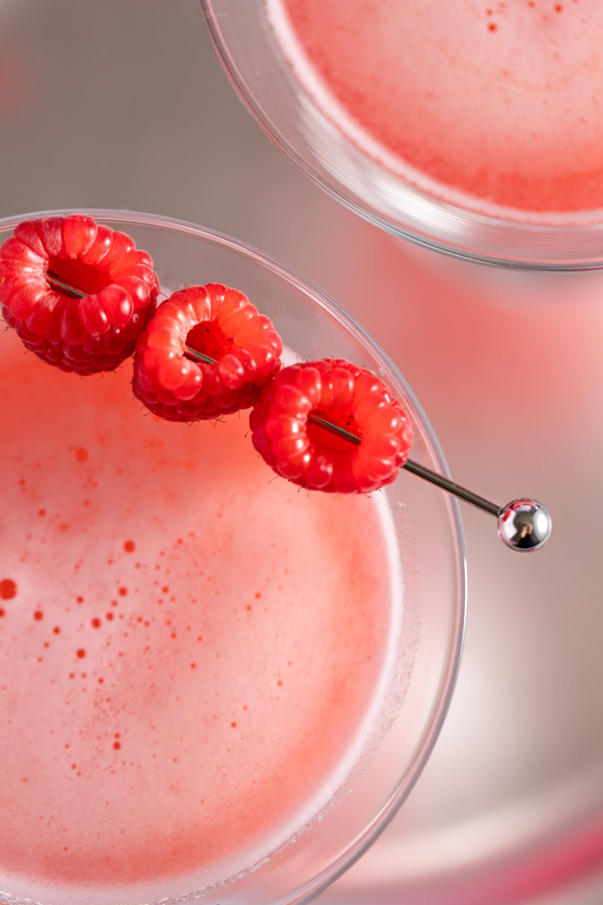 Up close view of the 3 raspberries garnishing a martini on a silver cocktail pick.
