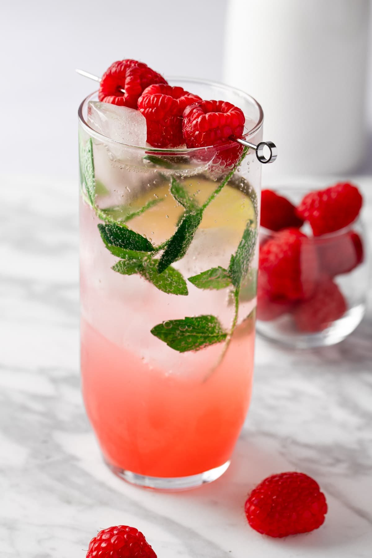 A raspberry mojito mocktail garnished with raspberries, on a white marble table.