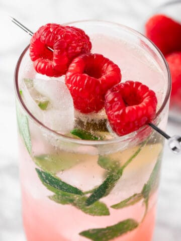 A raspberry mojito mocktail garnished with fresh raspberries and mint leaves.
