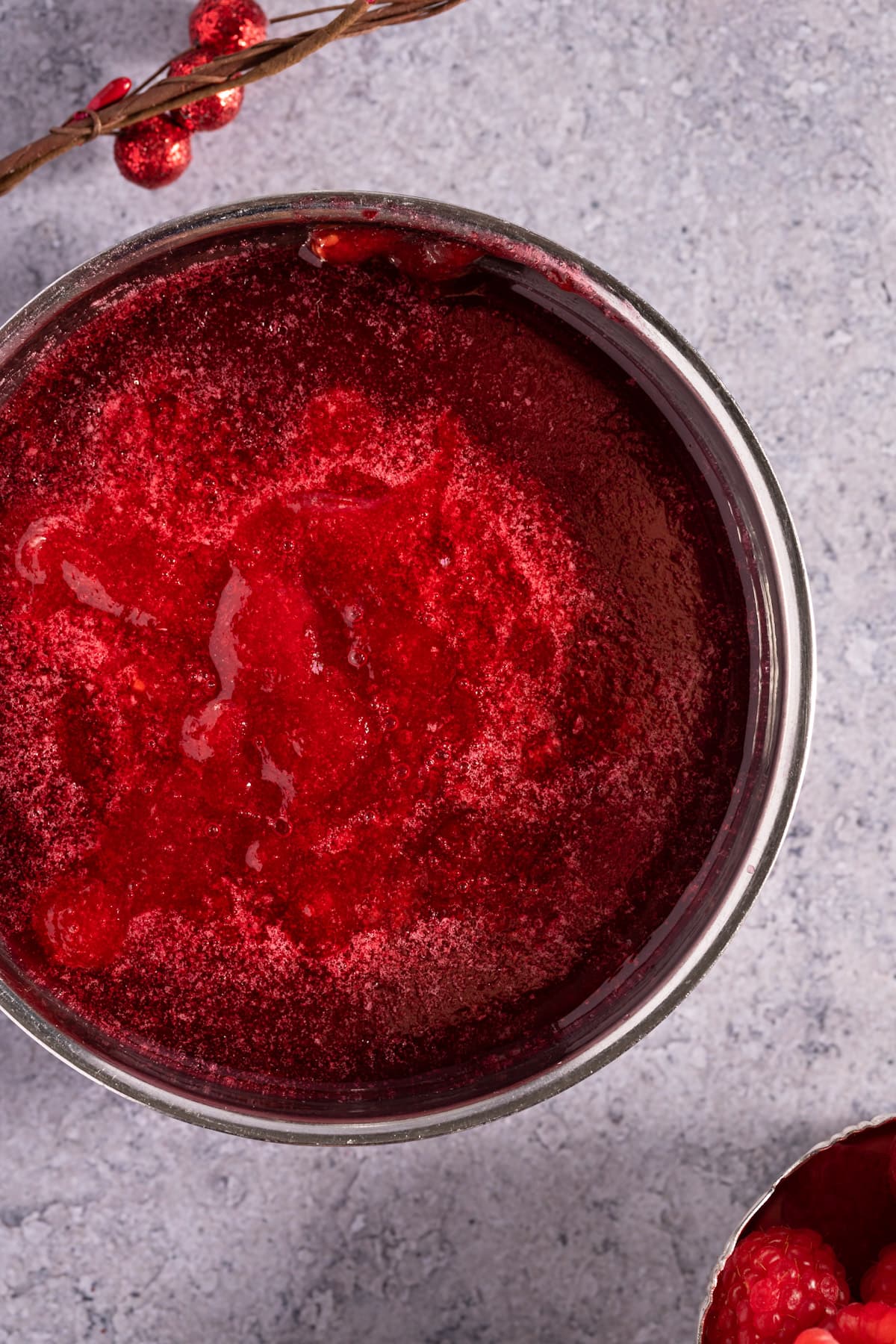 Overhead syrup of a bowl of red syrup, on a grey table.