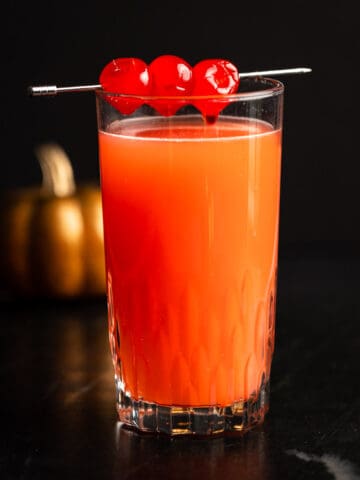 Red devil drink garnished with maraschino cherries, on a black marble table.