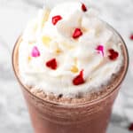 A red velvet frappuccino topped with whipped cream and heart sprinkles.