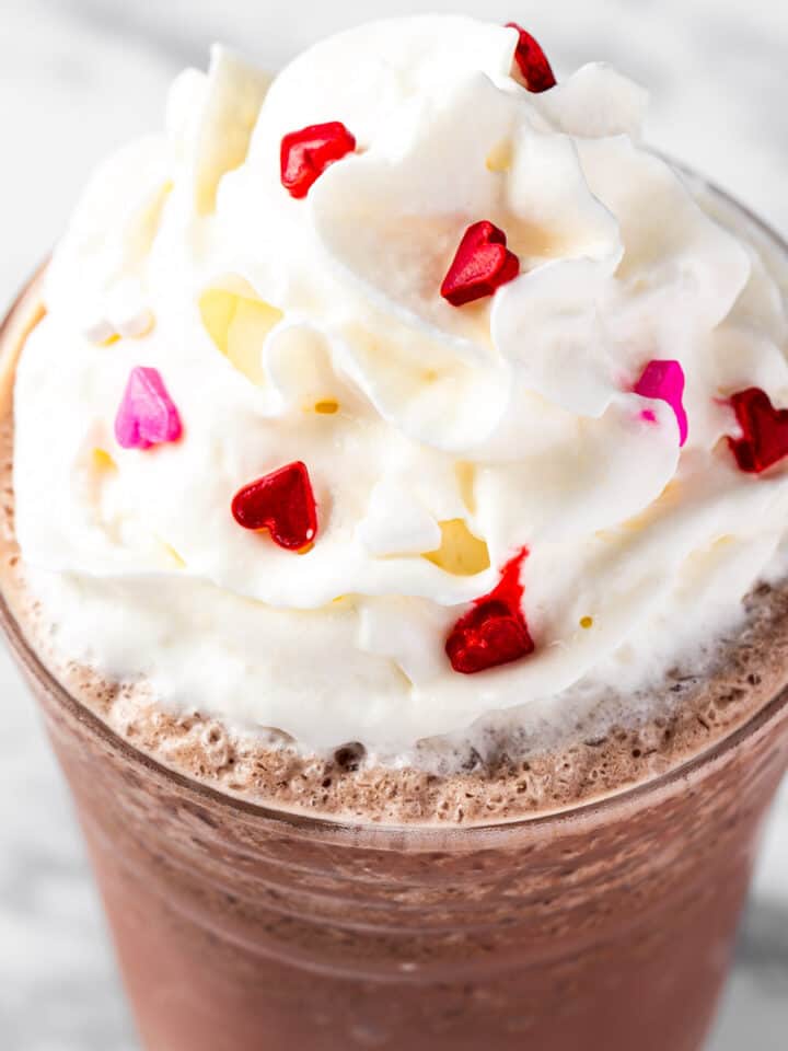 A red velvet frappuccino topped with whipped cream and heart sprinkles.