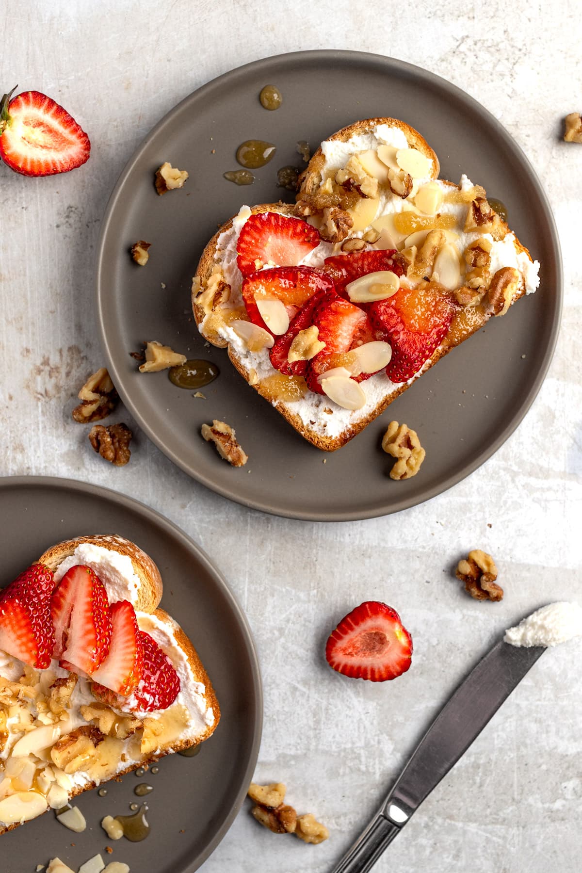 Honey and ricotta toast topped with nuts, and fresh sliced strawberries on a marble background.