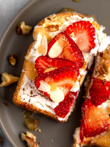 A slice of ricotta honey toast topped with ricotta, walnuts, almonds, strawberries and warm honey.