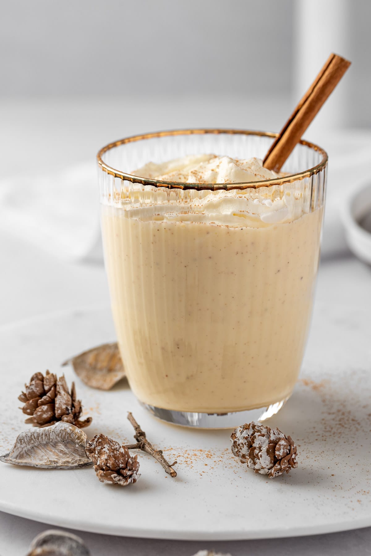 Eye level view of a rumchata and eggnog drink, garnished with a cinnamon stick, on a white background.