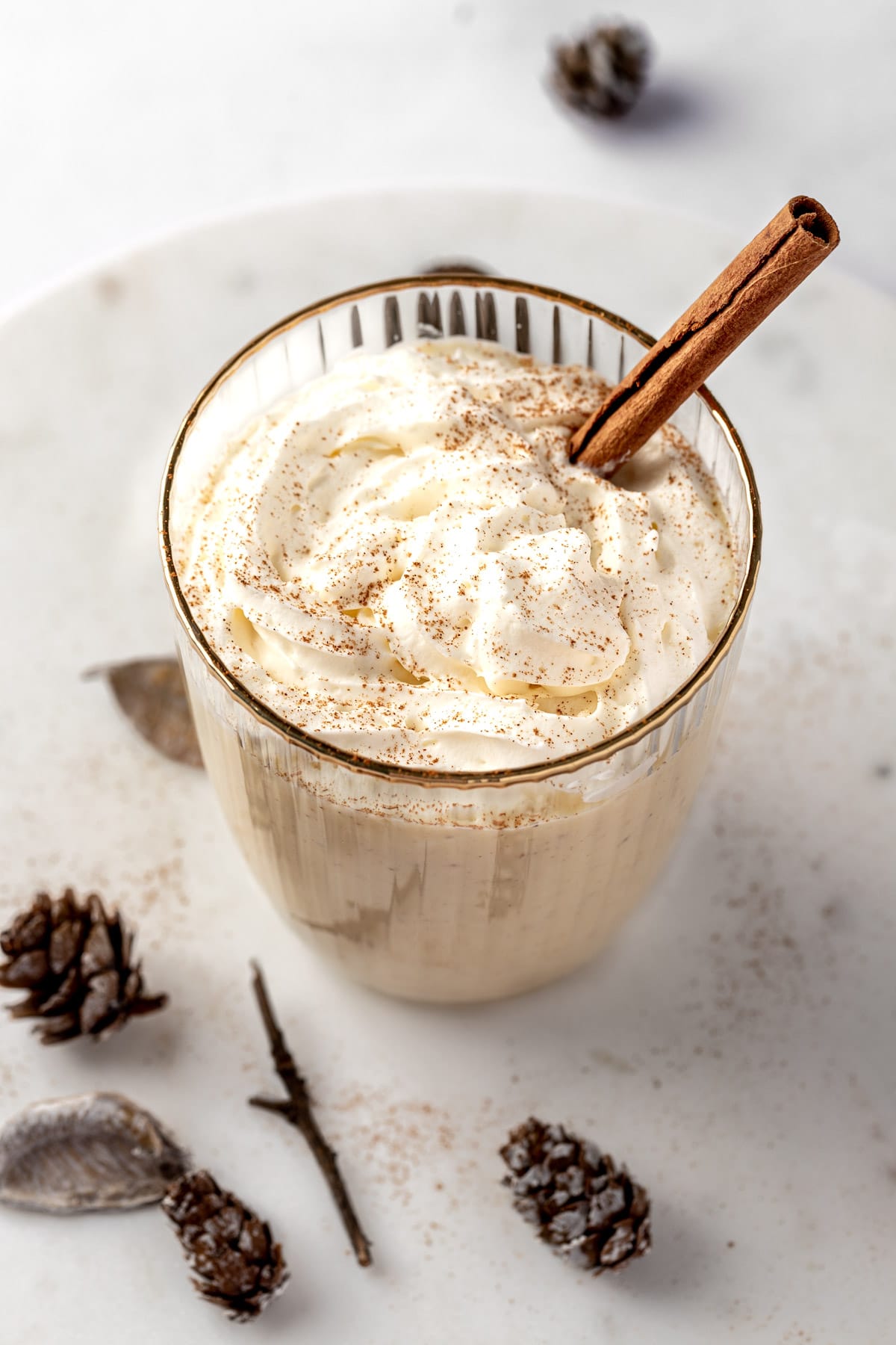 A RumChata eggnog cocktail topped with whipped cream, a sprinkle of nutmeg and a cinnamon stick.