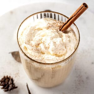 A RumChata eggnog cocktail topped with whipped cream, a sprinkle of nutmeg and a cinnamon stick.