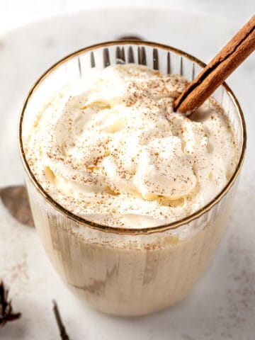 A RumChata eggnog cocktail topped with whipped cream, a sprinkle of nutmeg and a cinnamon stick.