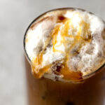 Salted caramel cold foam on top of a an iced coffee drink, with an extra drizzle of salted caramel sauce.
