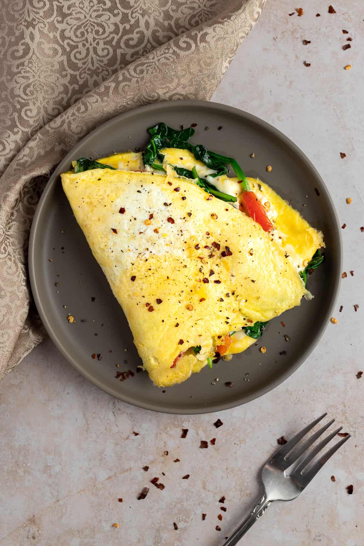 Overhead view of a feta spinach omelette topped with red pepper flakes, on a round brown plate.