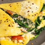 A close up view of a cheesy spinach and feta omelette cut in half.