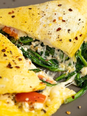 A close up view of a cheesy spinach and feta omelette cut in half.