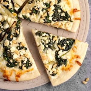 A slice of spinach and feta pizza fresh out of the oven, served on a pizza stone.