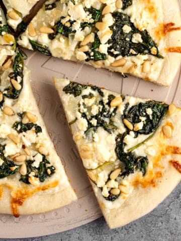A slice of spinach and feta pizza fresh out of the oven, served on a pizza stone.