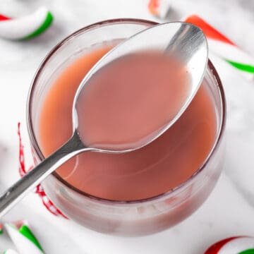 A spoonful of purple-pink Starbucks peppermint syrup, on a white marble table with candy cane pieces.