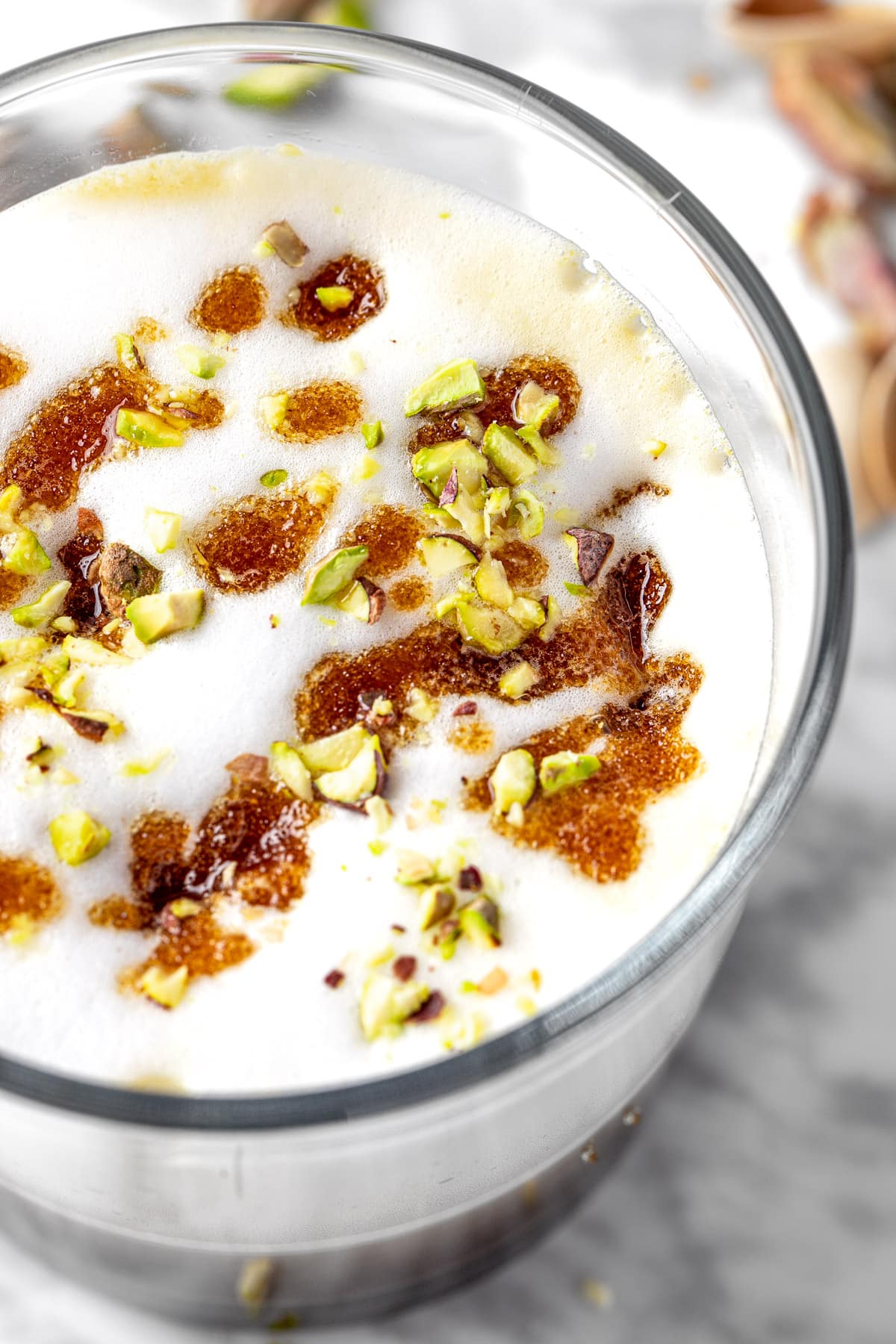 Up close view of a pistachio latte topped with milk foam, brown sugar topping and crushed, green pistachios.