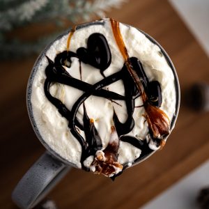 Overhead view of a starbucks salted caramel latte with whipped cream, caramel and chocolate drizzle on top, sitting on a wooden board.