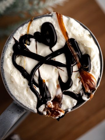 Overhead view of a starbucks salted caramel latte with whipped cream, caramel and chocolate drizzle on top, sitting on a wooden board.