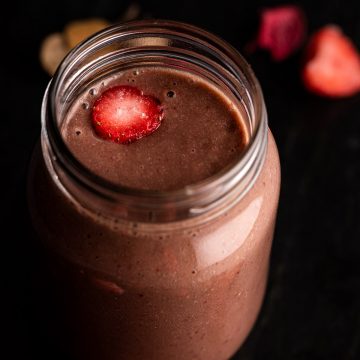 Close up view of a strawberry banana chocolate smoothie in a mason jar, on a black marble board.