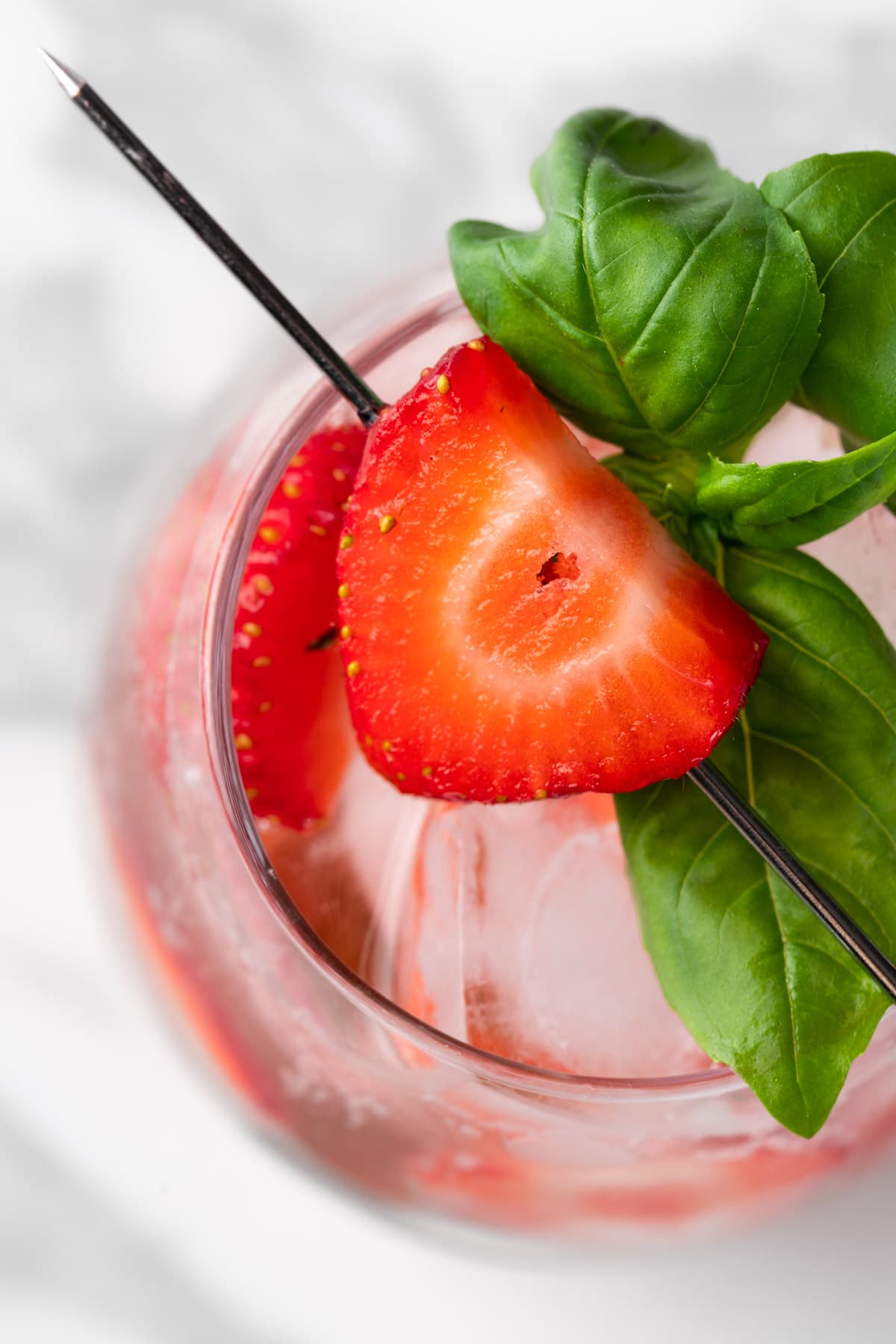Overhead view of a strawberry basil mocktail garnished with strawberries and basil leaves.