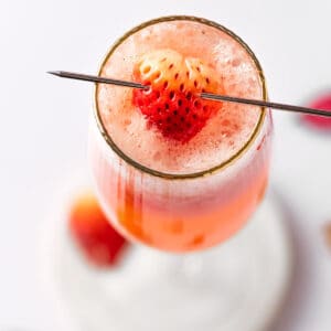 A strawberry bellini with Prosecco, garnished with a strawberry slice, on a white table.