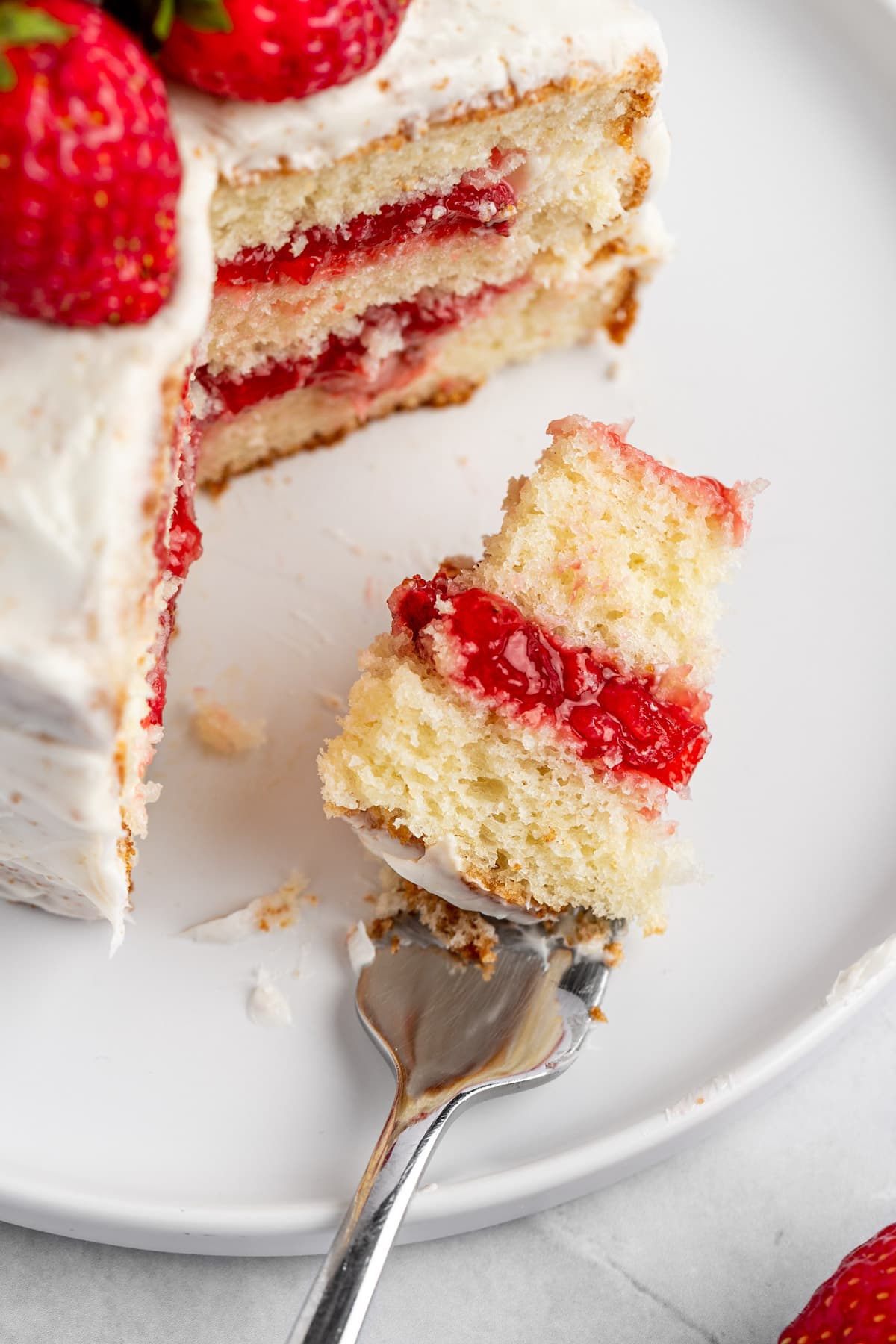 A fork with a bite of white cake with red strawberry layers.