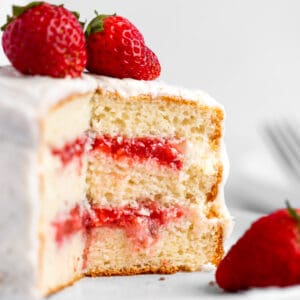 A white layered cake cut in half, filled with layers of strawberry cake filling.
