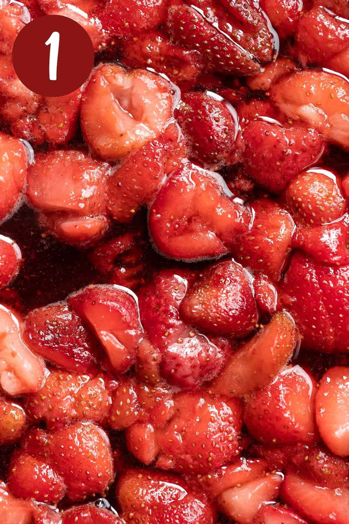 Close up view of strawberries, lemon juice and sugar cooking in a pan on the stovetop.