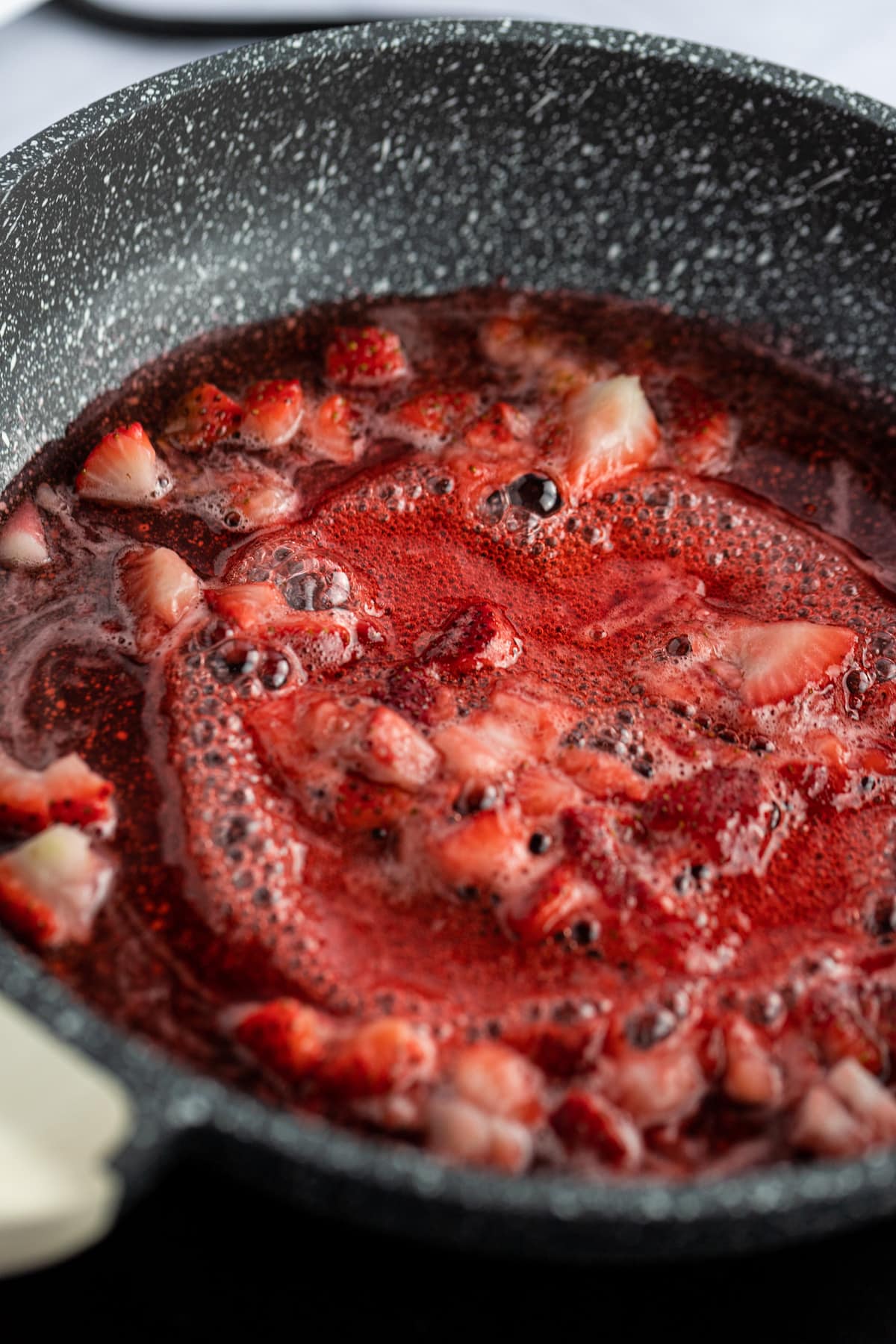 Close up photo of red strawberry syrup simmering on a saucepan.