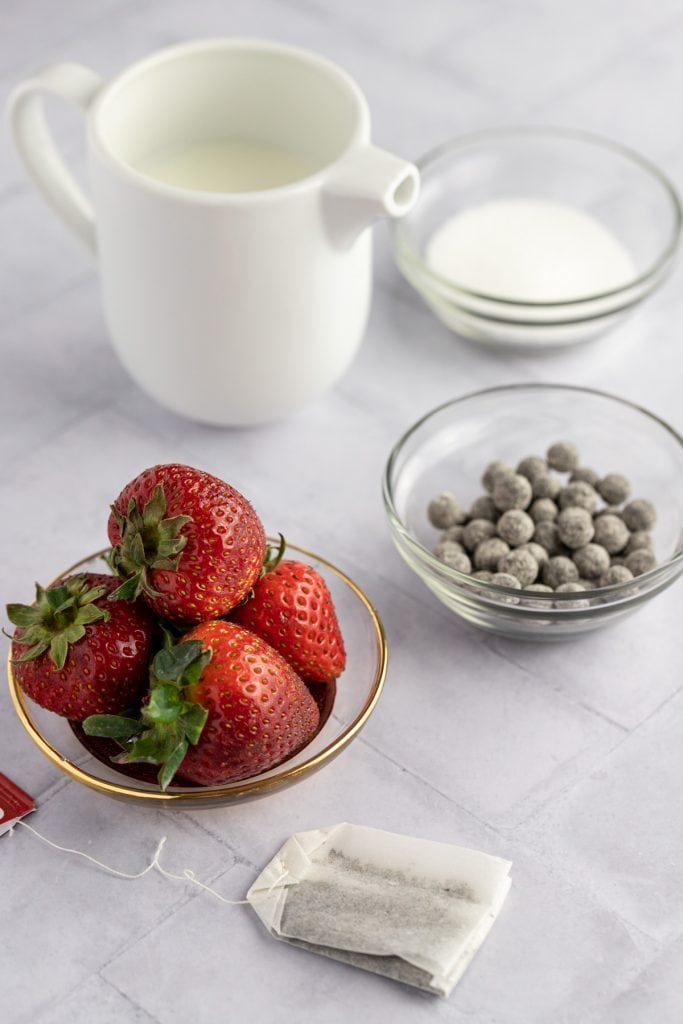 Ingredients shot of fresh strawberries, a tea bag, uncooked boba, milk and sugar.