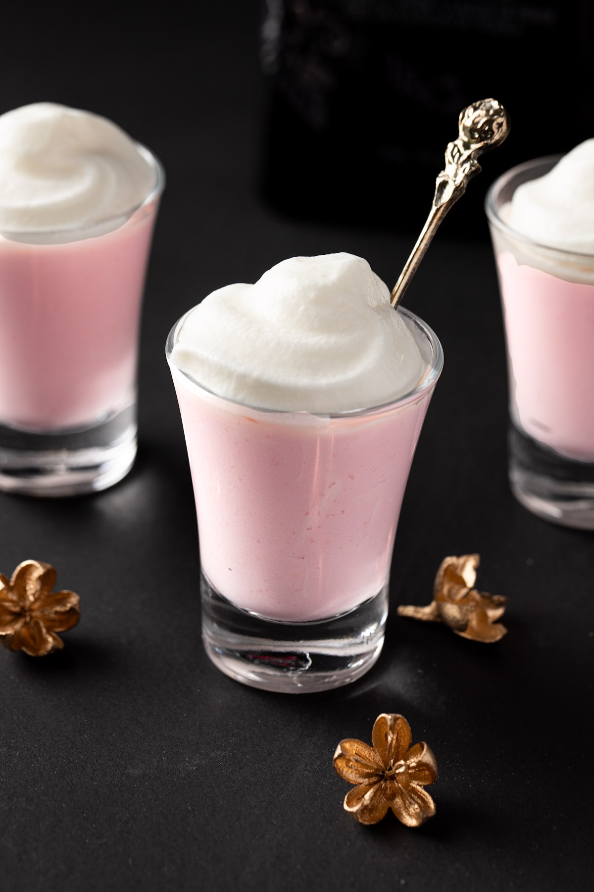Strawberry pudding shots topped with whipped cream, on a black table.