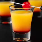 Three Tequila Sunrise Shots garnished with a maraschino cherry on a black background.