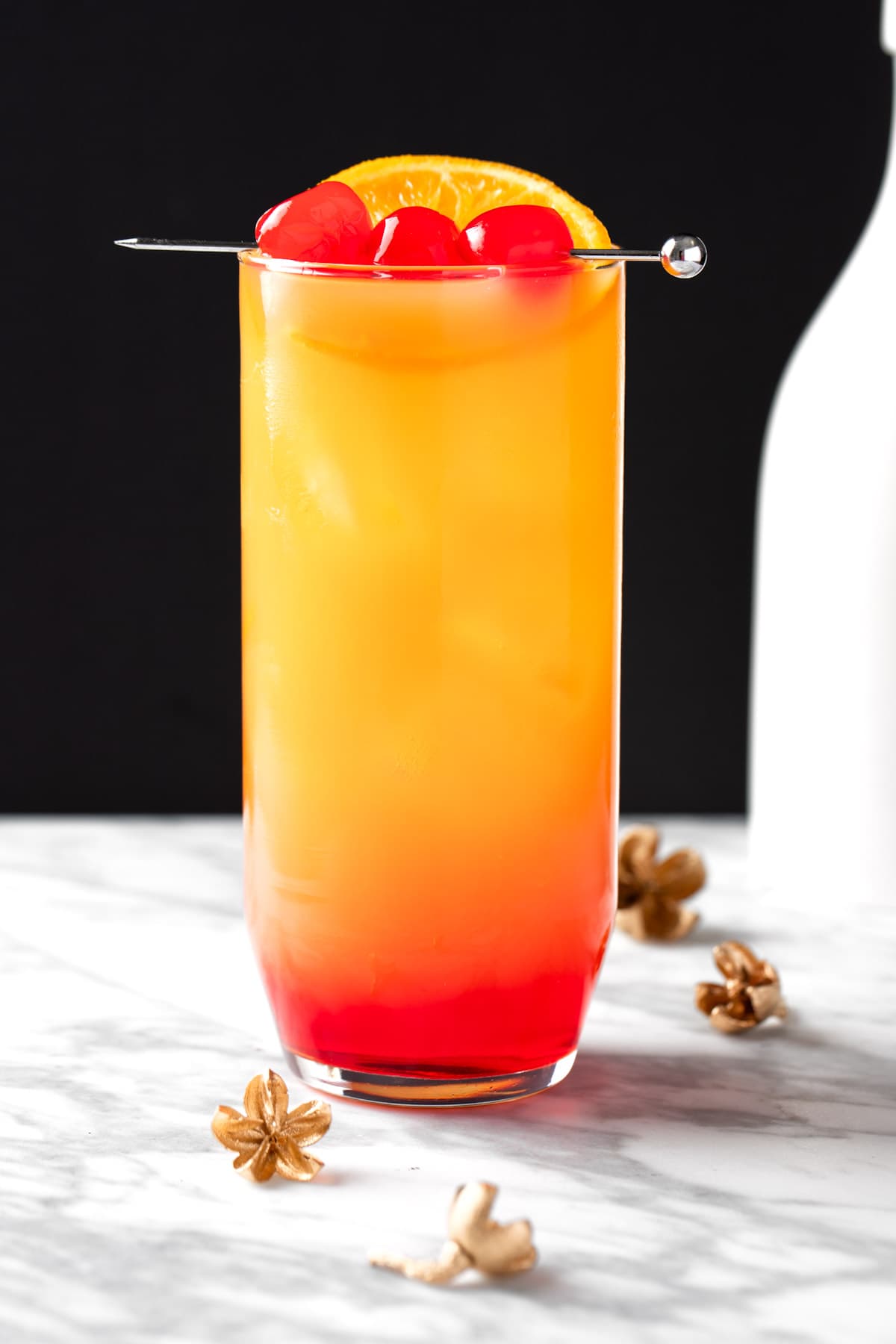 A tequila sunrise made with strawberry syrup on a white and black background.