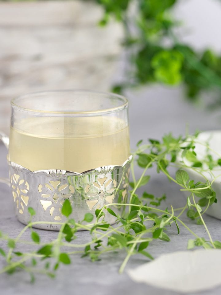 A small glass of thyme simple syrup in a lace metal holder, next to fresh thyme.