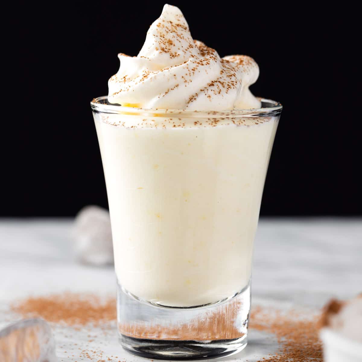 A vanilla pudding shot topped with whipped cream.