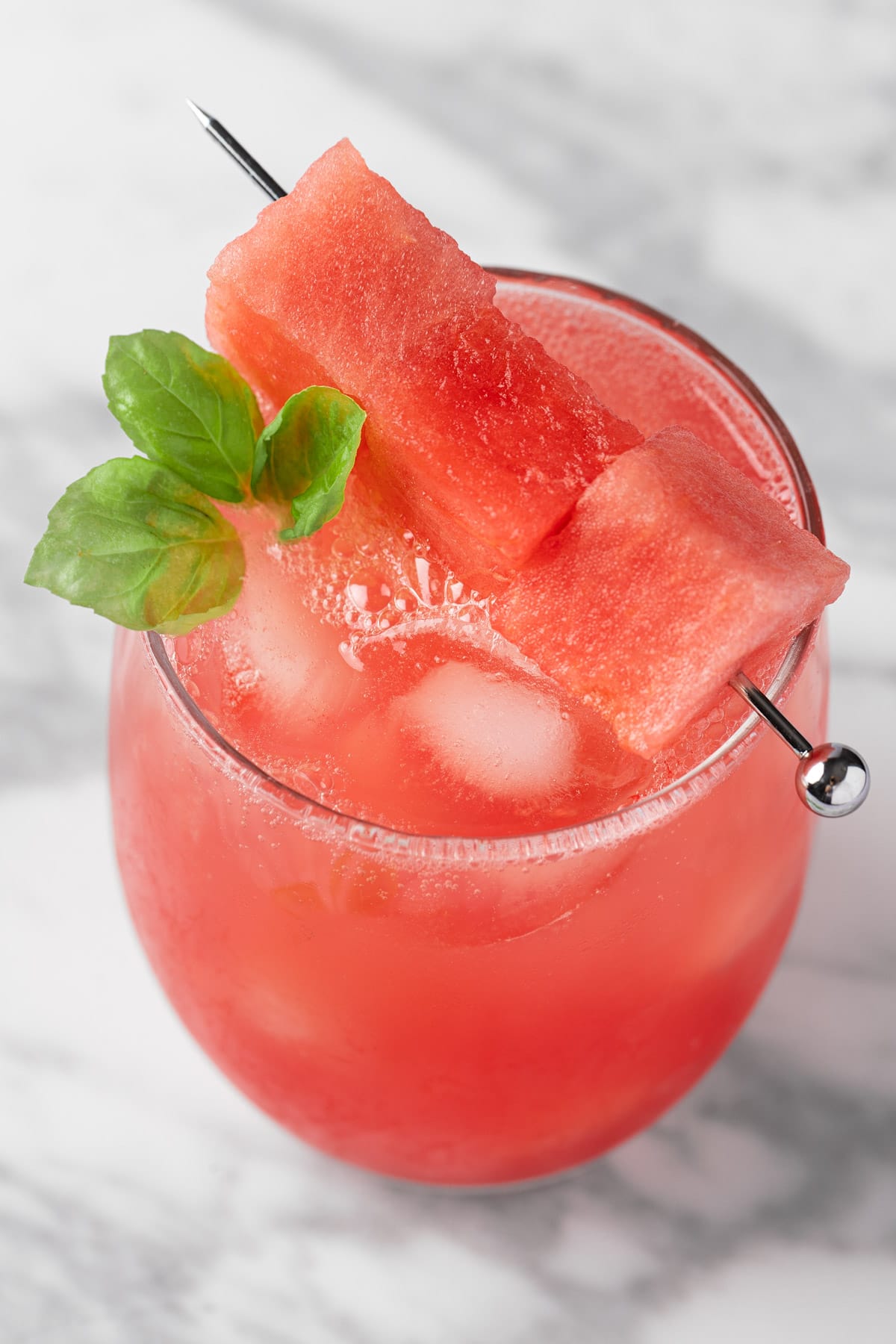 A watermelon basil mocktail garnished with watermelon chunks and basil leaves.