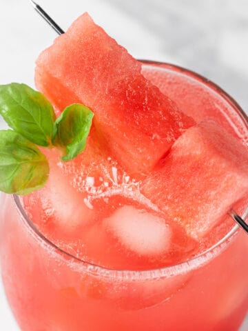 A watermelon basil mocktail garnished with watermelon chunks and basil leaves.