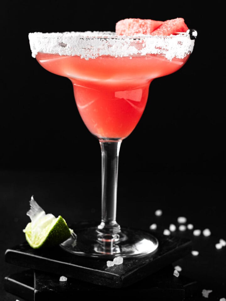A pink watermelon margarita on the rocks, with a black background.