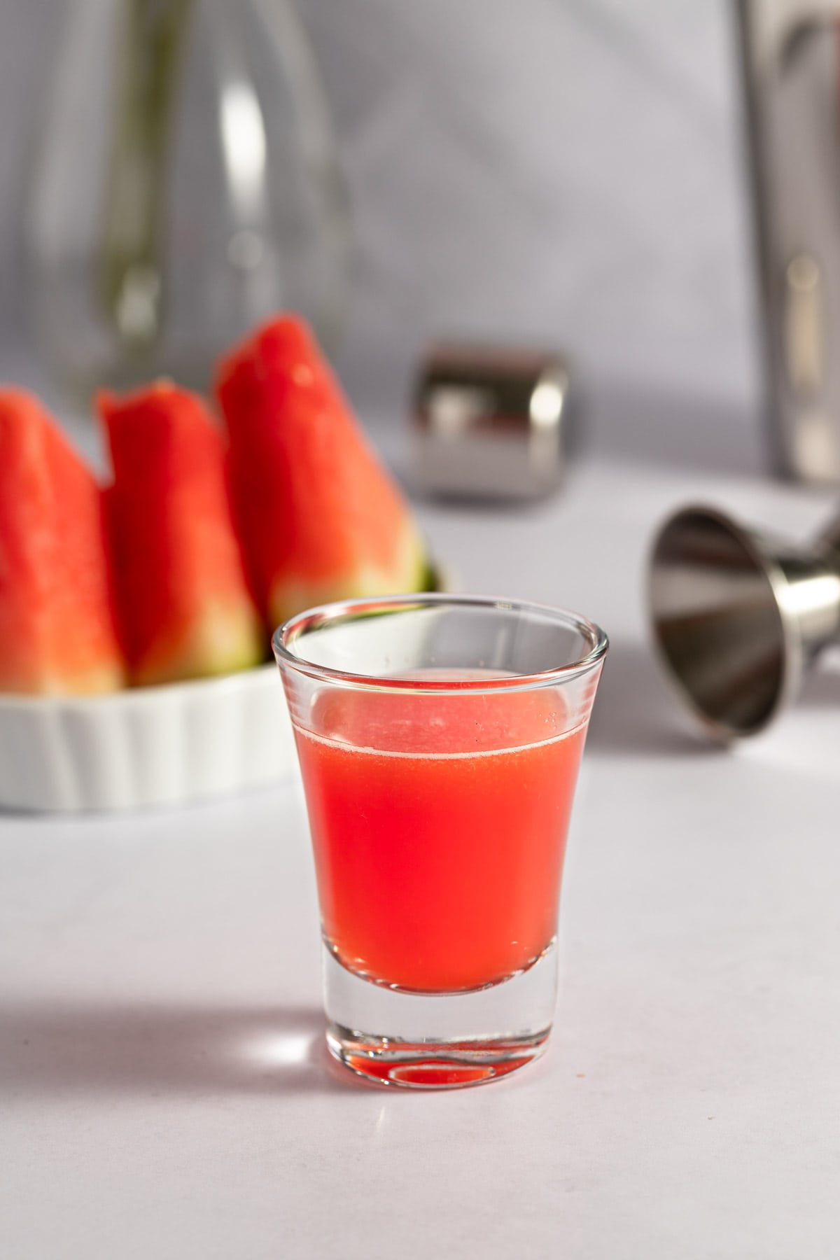 Up close photo of a pinkish-red watermelon shot, with a small plate of sliced watermelon in the background.