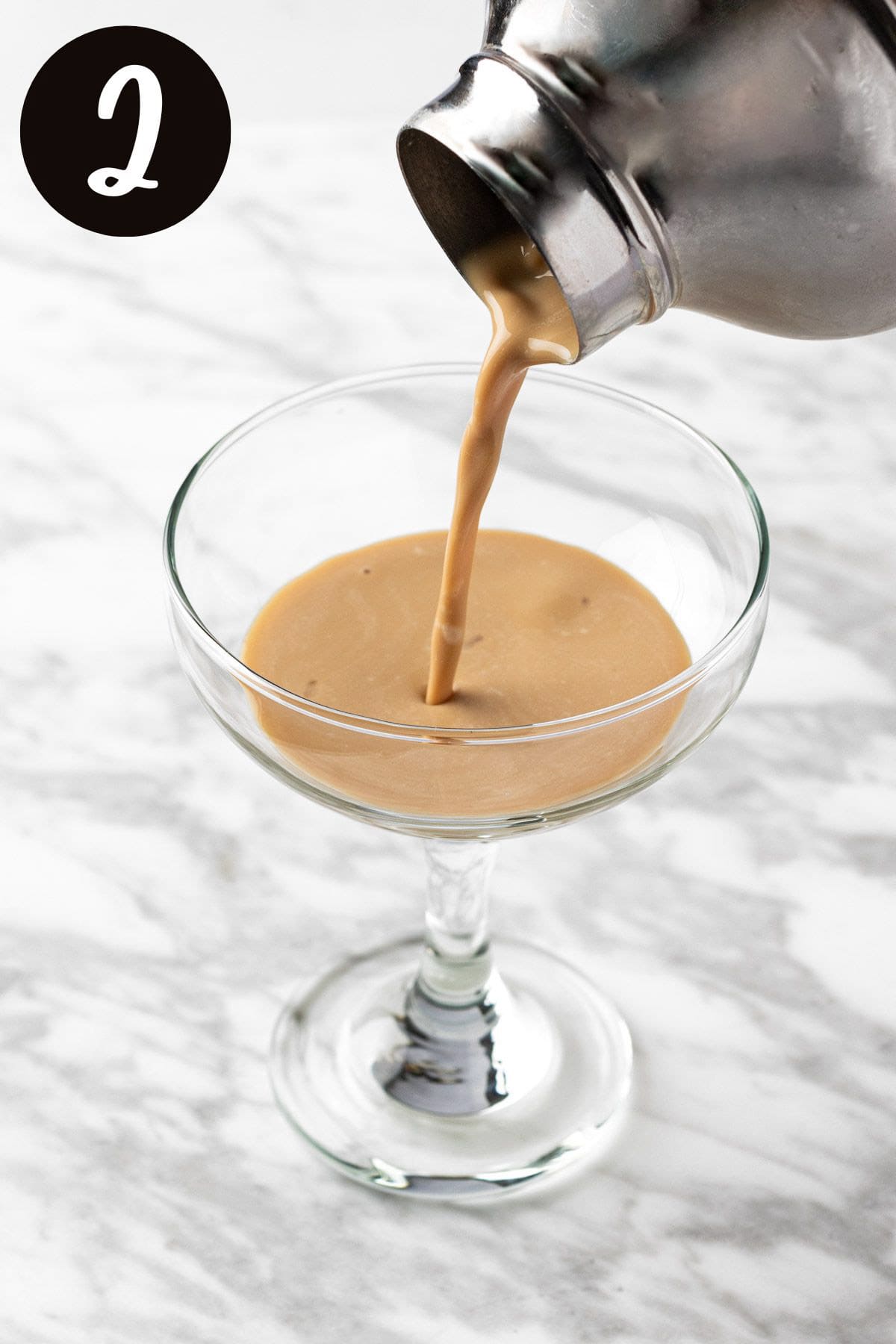 Pouring the white chocolate espresso martini from the cocktail shaker into a cocktail glass.